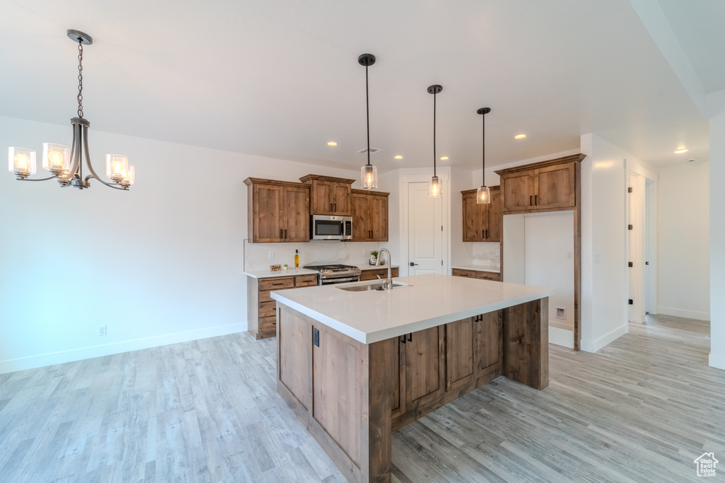 Kitchen with light wood-type flooring, an island with sink, a notable chandelier, decorative light fixtures, and appliances with stainless steel finishes