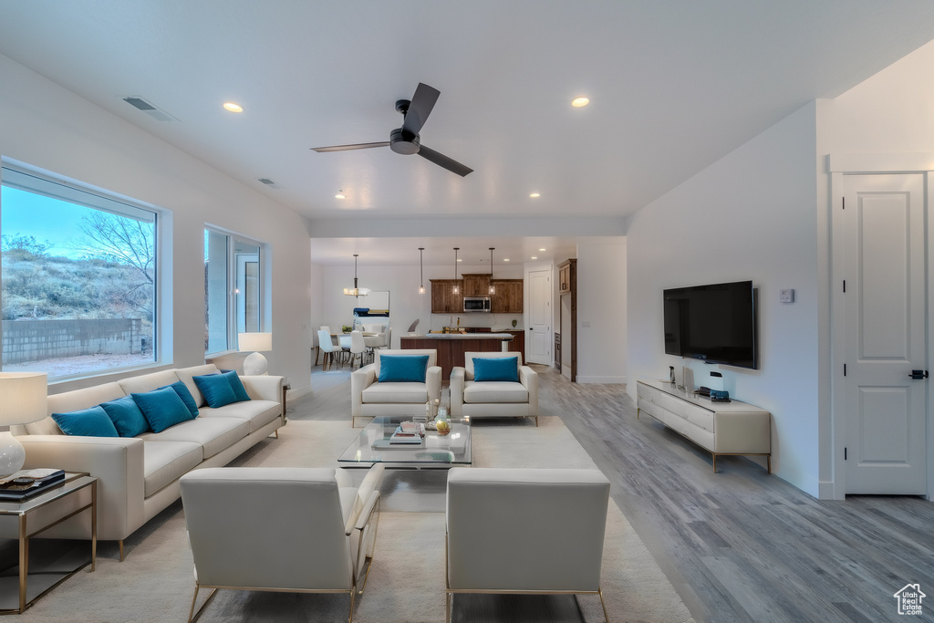 Living room with light hardwood / wood-style floors and ceiling fan with notable chandelier