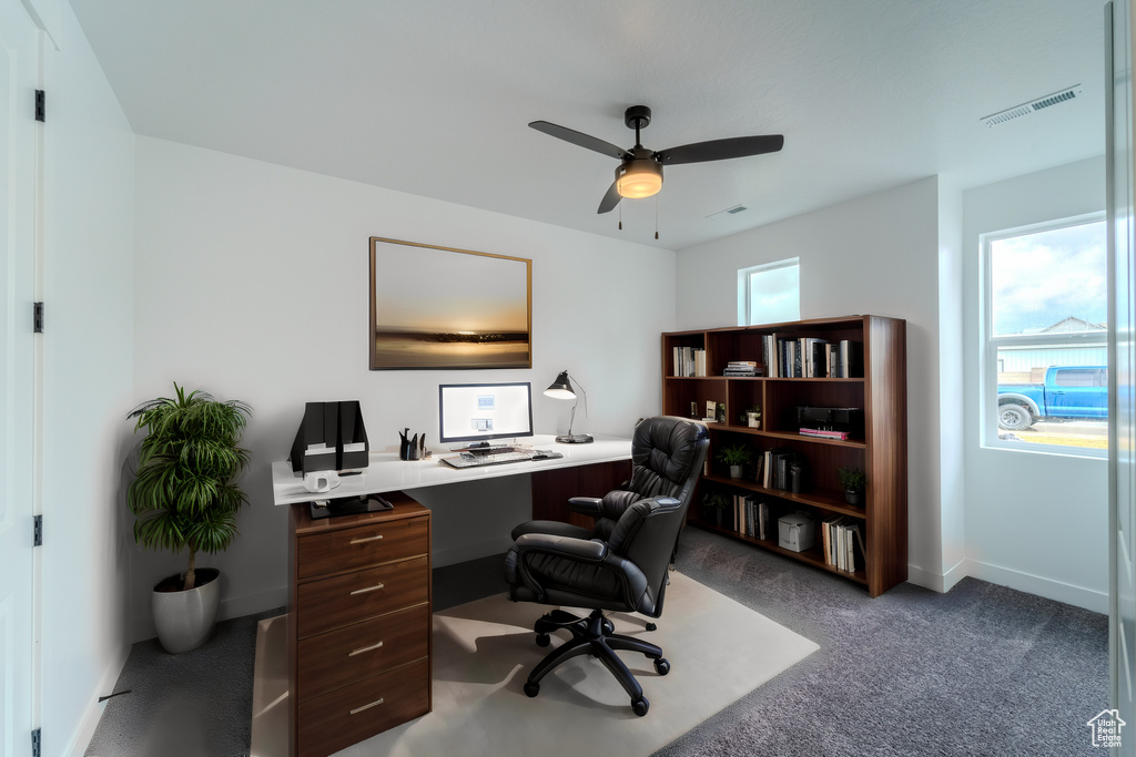 Office with dark carpet, ceiling fan, and a healthy amount of sunlight