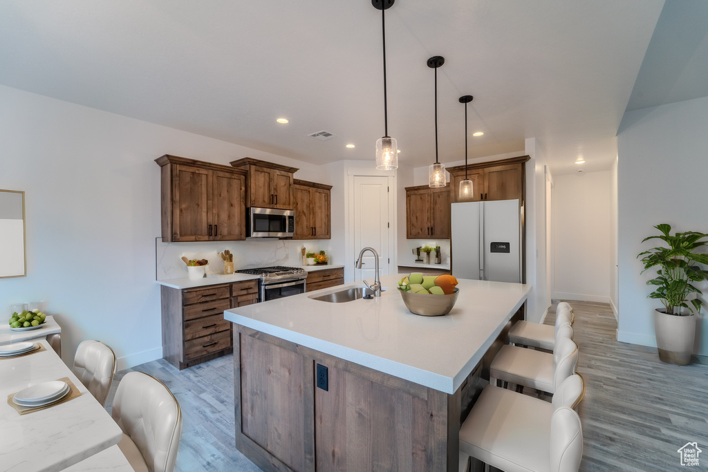 Kitchen featuring light wood-type flooring, stainless steel appliances, a breakfast bar, sink, and decorative light fixtures