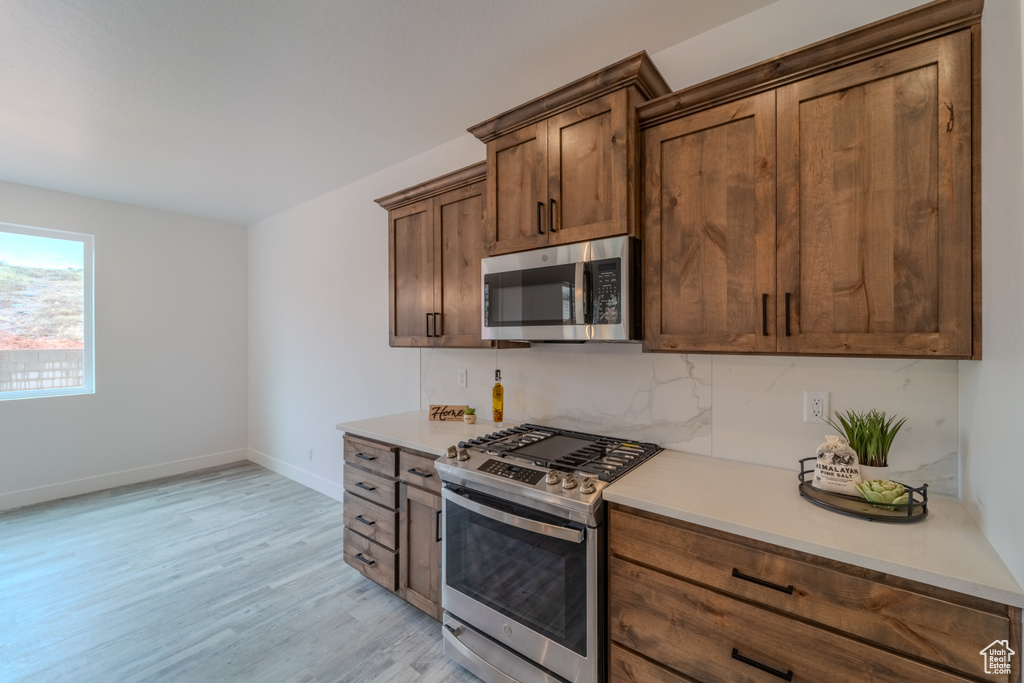 Kitchen with light hardwood / wood-style flooring, stainless steel appliances, and backsplash