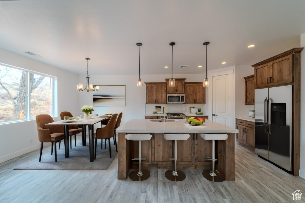 Kitchen featuring light wood-type flooring, hanging light fixtures, an island with sink, stainless steel appliances, and a chandelier