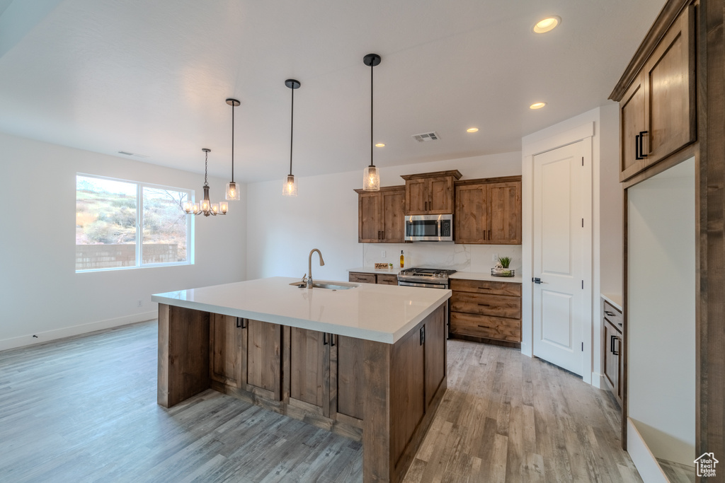Kitchen with pendant lighting, an inviting chandelier, stainless steel appliances, light hardwood / wood-style flooring, and sink