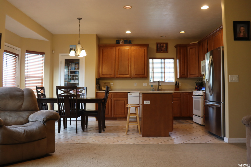 Kitchen featuring decorative light fixtures, light carpet, brown cabinets, light countertops, and white appliances