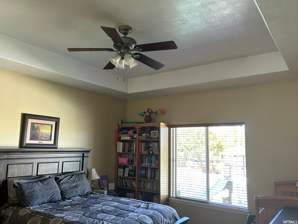 Bedroom with a raised ceiling, a textured ceiling, and ceiling fan