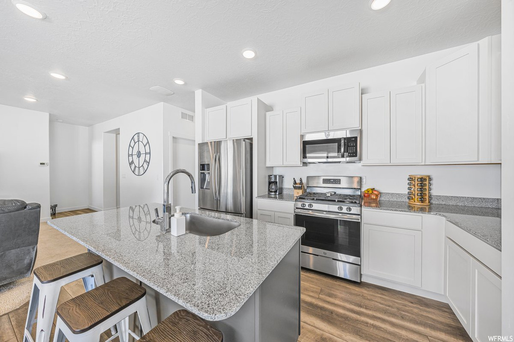 Kitchen featuring white cabinets, light hardwood floors, appliances with stainless steel finishes, a center island, and light stone countertops