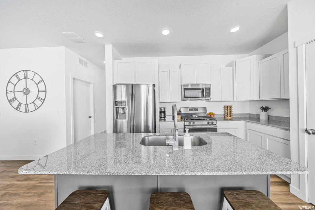 Kitchen with light stone counters, appliances with stainless steel finishes, light hardwood floors, and white cabinetry