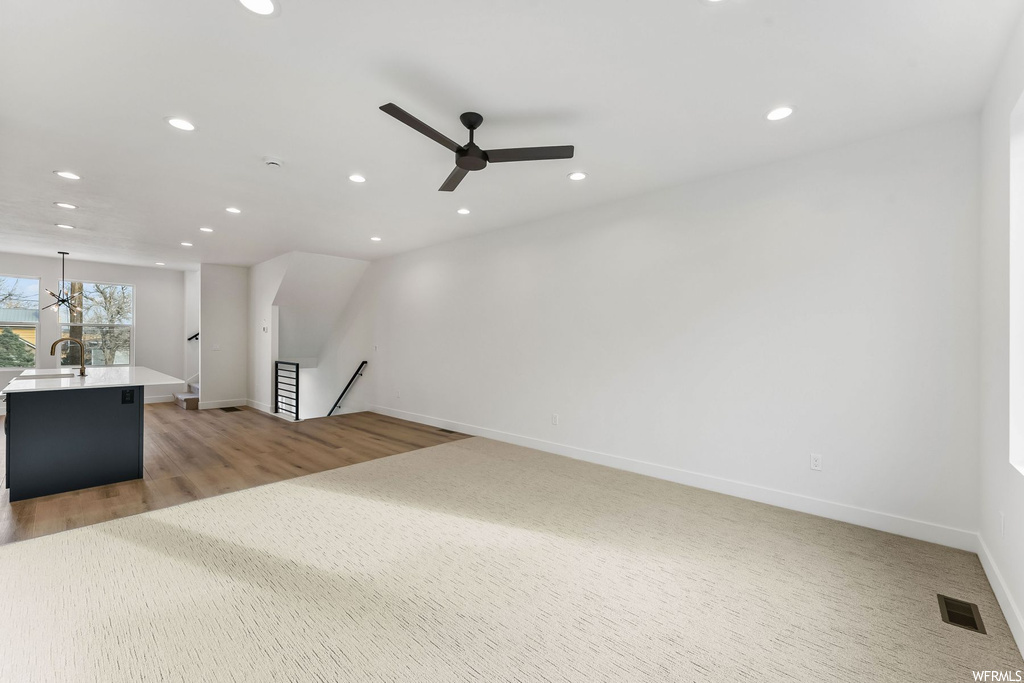 Unfurnished living room featuring sink, light wood-type flooring, and ceiling fan with notable chandelier