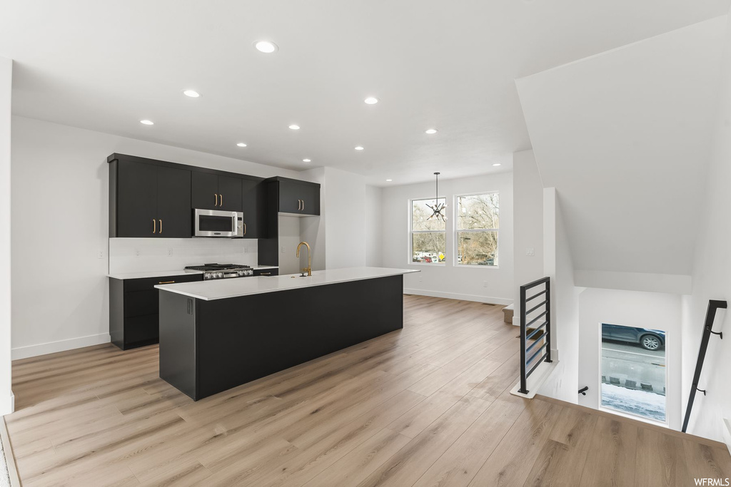 Kitchen featuring light hardwood / wood-style flooring, a kitchen island with sink, an inviting chandelier, decorative light fixtures, and backsplash