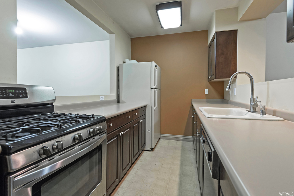 Kitchen with white fridge, light countertops, light tile floors, dark brown cabinetry, and stainless steel gas range oven