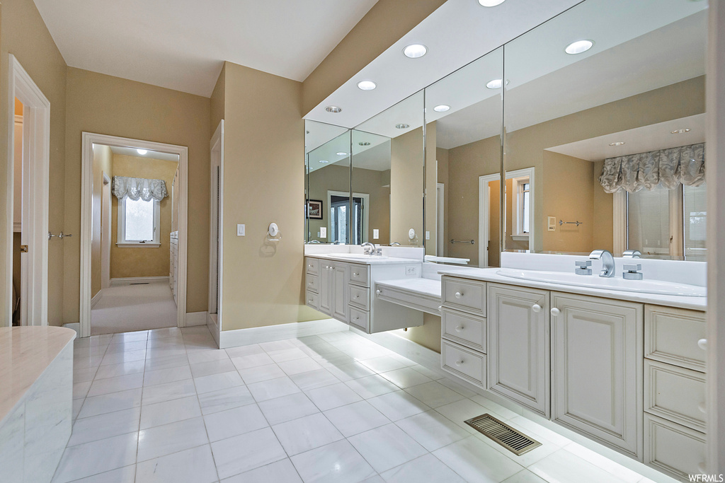 Bathroom featuring dual large vanity, light tile flooring, and mirror