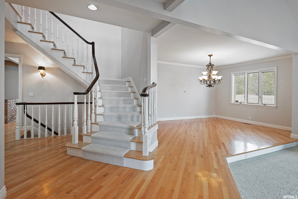 Stairs with crown molding, a chandelier, beamed ceiling, and light hardwood flooring