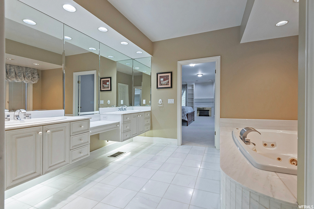 Bathroom with dual large bowl vanity, mirror, a fireplace, tiled bath, and light tile floors