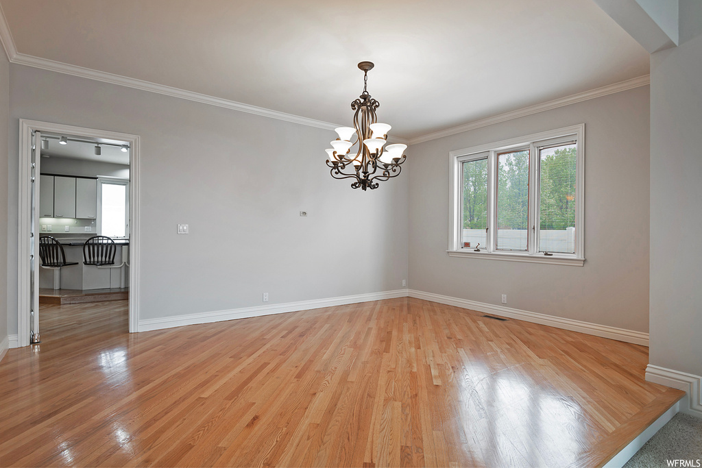 Empty room with crown molding, a notable chandelier, and light hardwood floors
