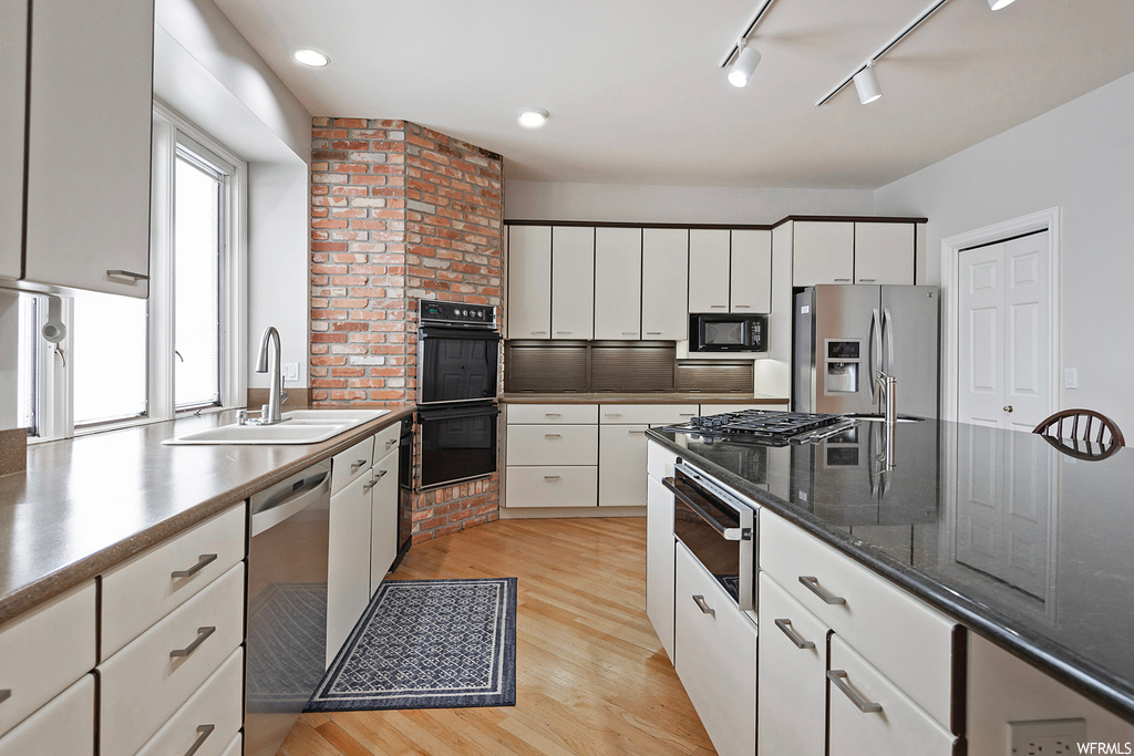 Kitchen featuring white cabinets, brick wall, black appliances, hardwood flooring, rail lighting, and dark countertops