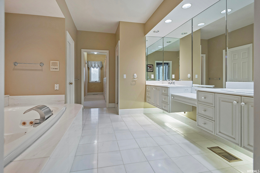 Bathroom featuring tiled tub, large vanity, mirror, and light tile floors