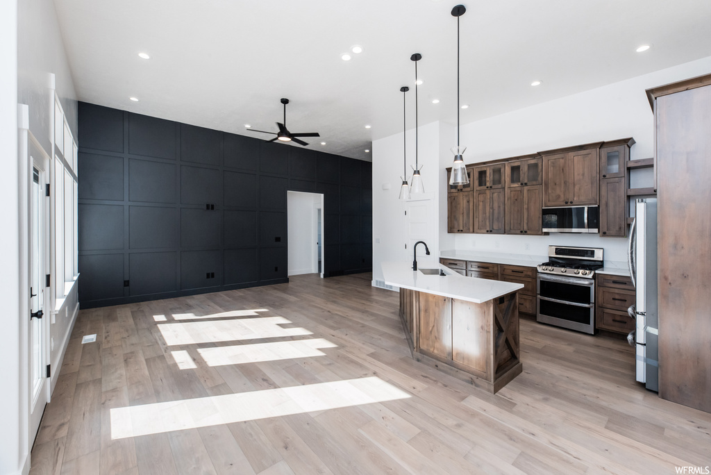 Kitchen featuring decorative light fixtures, dark brown cabinets, light countertops, light hardwood floors, and appliances with stainless steel finishes