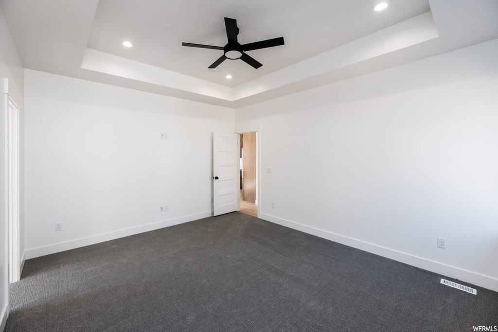 Empty room featuring a tray ceiling, carpet, and ceiling fan