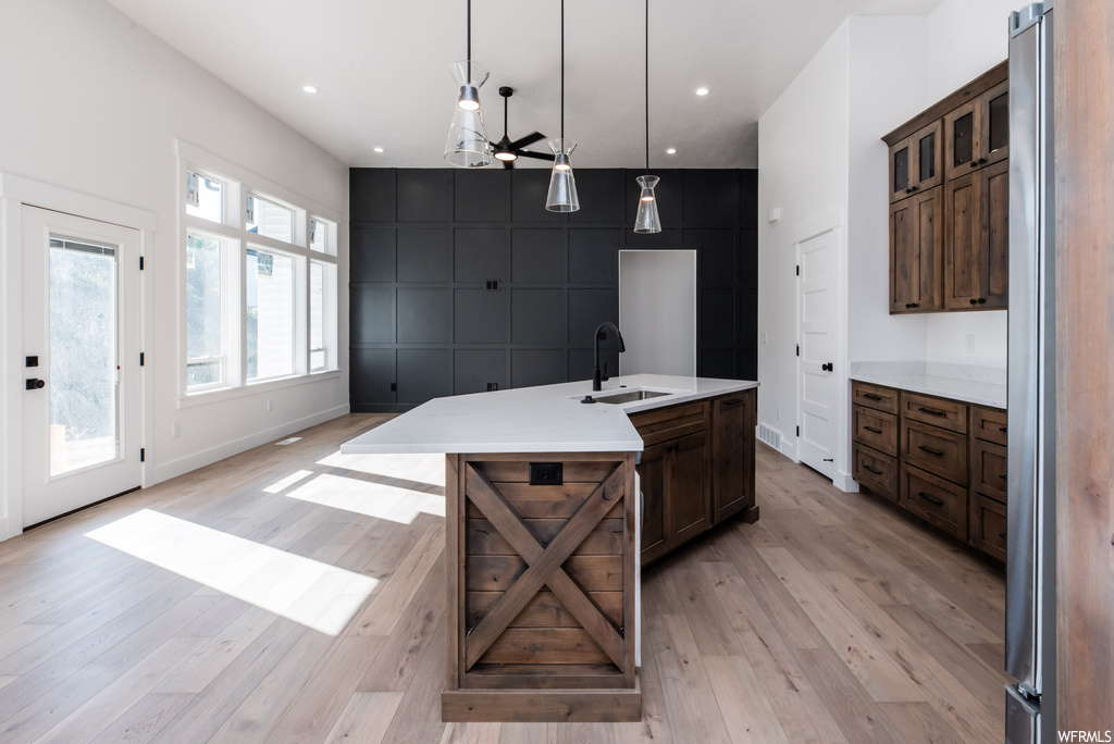Kitchen with decorative light fixtures, stainless steel fridge, light countertops, dark brown cabinets, and light hardwood floors