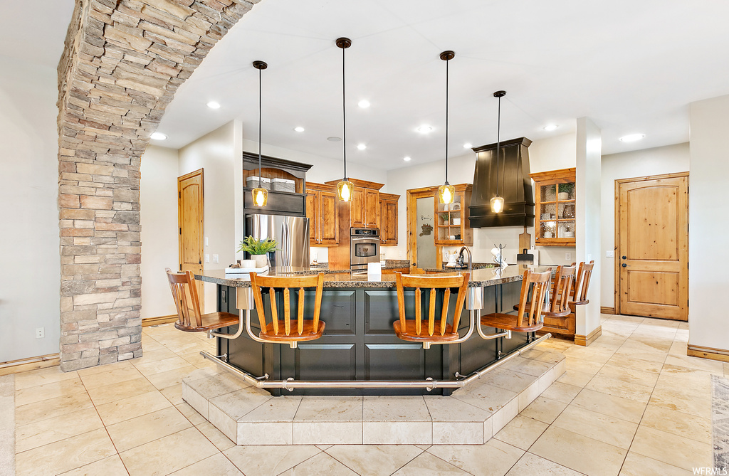 Kitchen with appliances with stainless steel finishes, a kitchen island, pendant lighting, light tile flooring, and custom exhaust hood