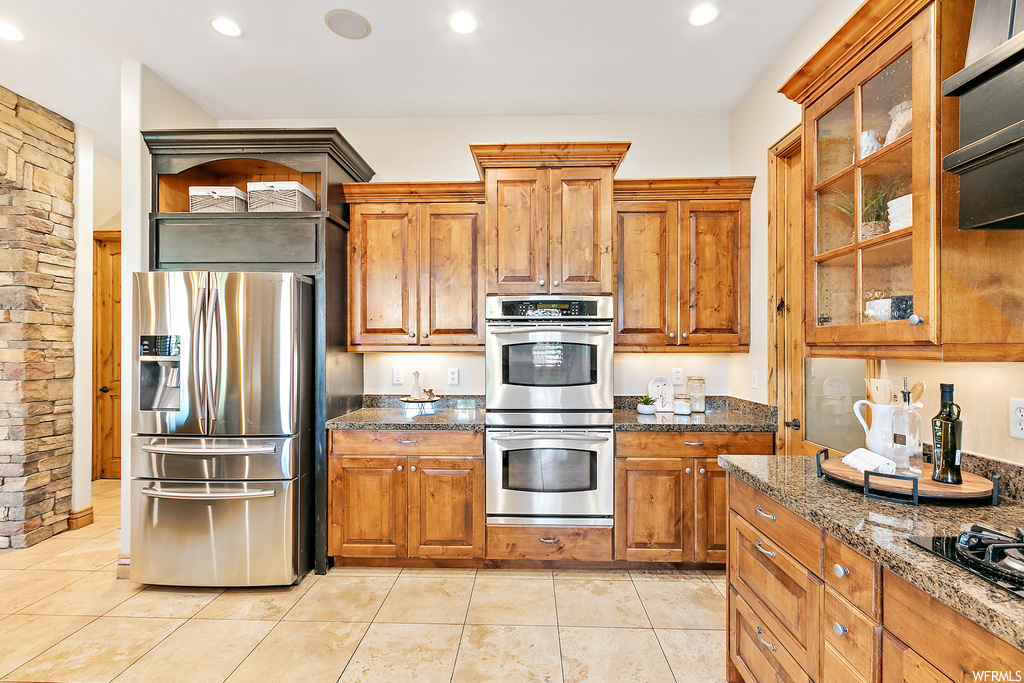 Kitchen featuring dark countertops, brown cabinets, stainless steel appliances, and light tile floors
