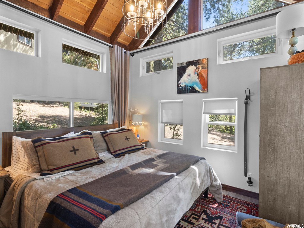 Bedroom featuring a notable chandelier, multiple windows, wood ceiling, vaulted ceiling with beams, and a high ceiling