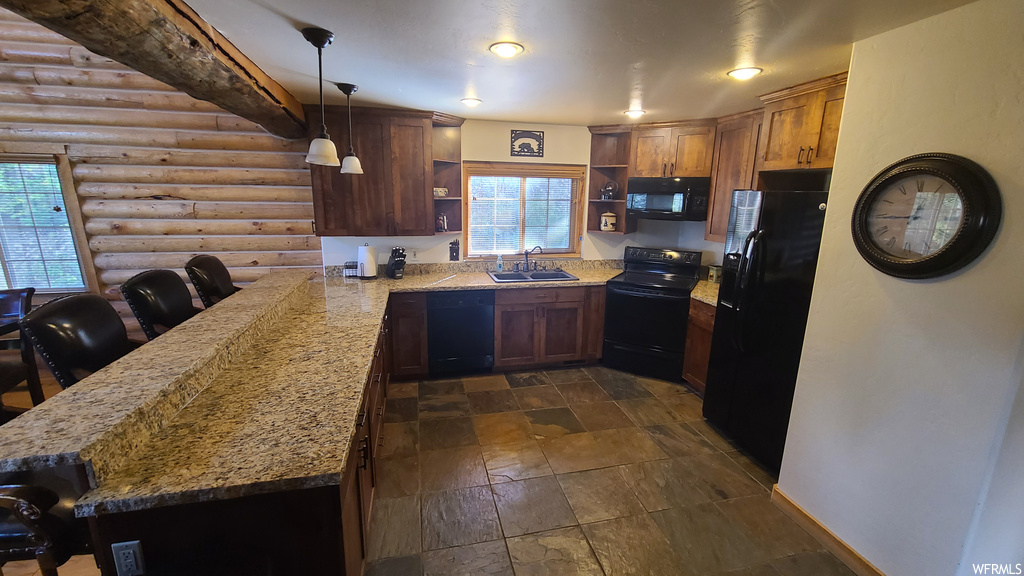 Kitchen featuring black appliances, log walls, dark tile flooring, light stone countertops, and a healthy amount of sunlight