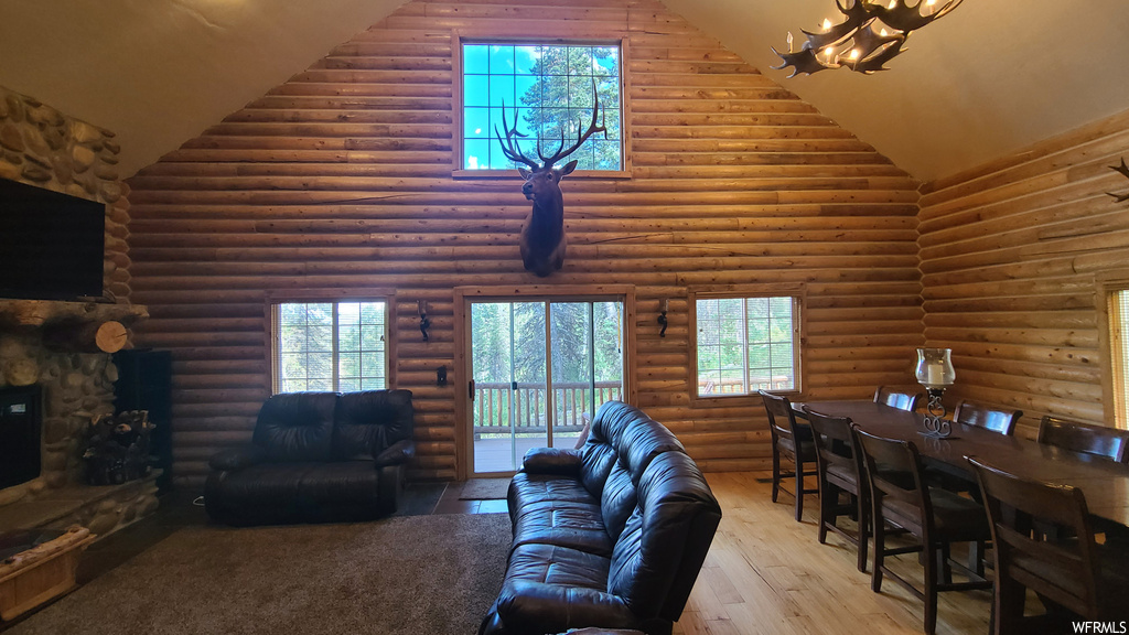 Living room featuring log walls, lofted ceiling, a fireplace, a healthy amount of sunlight, light hardwood flooring, and a high ceiling
