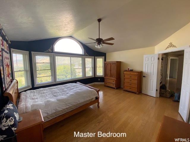 Bedroom featuring multiple windows, light hardwood flooring, vaulted ceiling, and ceiling fan
