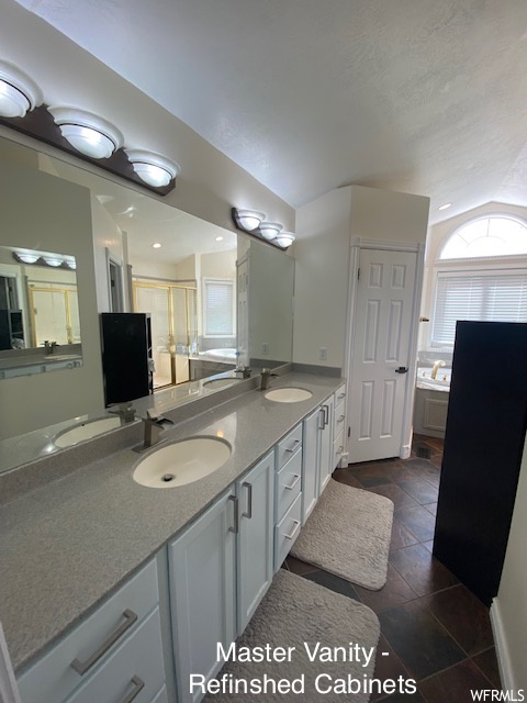 Bathroom with dark tile flooring, vaulted ceiling, double sink vanity, and mirror