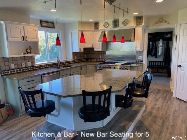 Kitchen featuring stainless steel dishwasher, a kitchen island, pendant lighting, dark stone countertops, range, hardwood floors, track lighting, and backsplash