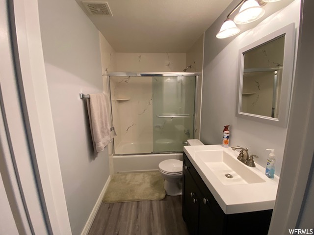 Full bathroom featuring enclosed tub / shower combo, large vanity, wood-type flooring, and toilet