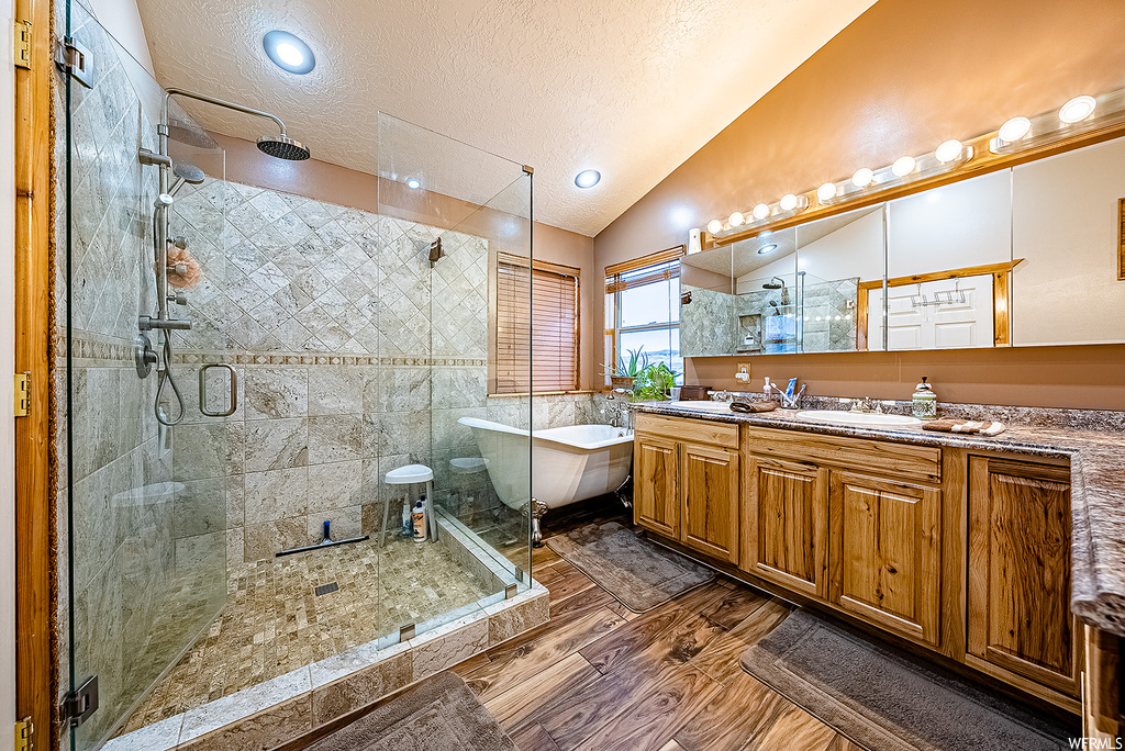 Bathroom with vaulted ceiling, a textured ceiling, hardwood flooring, double vanity, and shower with separate bathtub