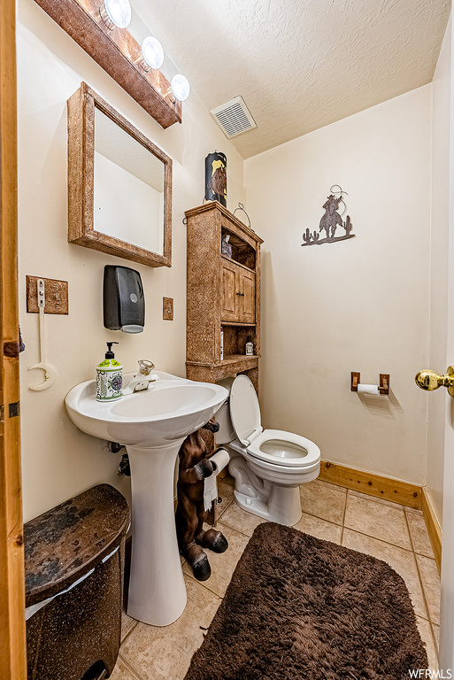 Bathroom with a textured ceiling, toilet, tile flooring, and washbasin