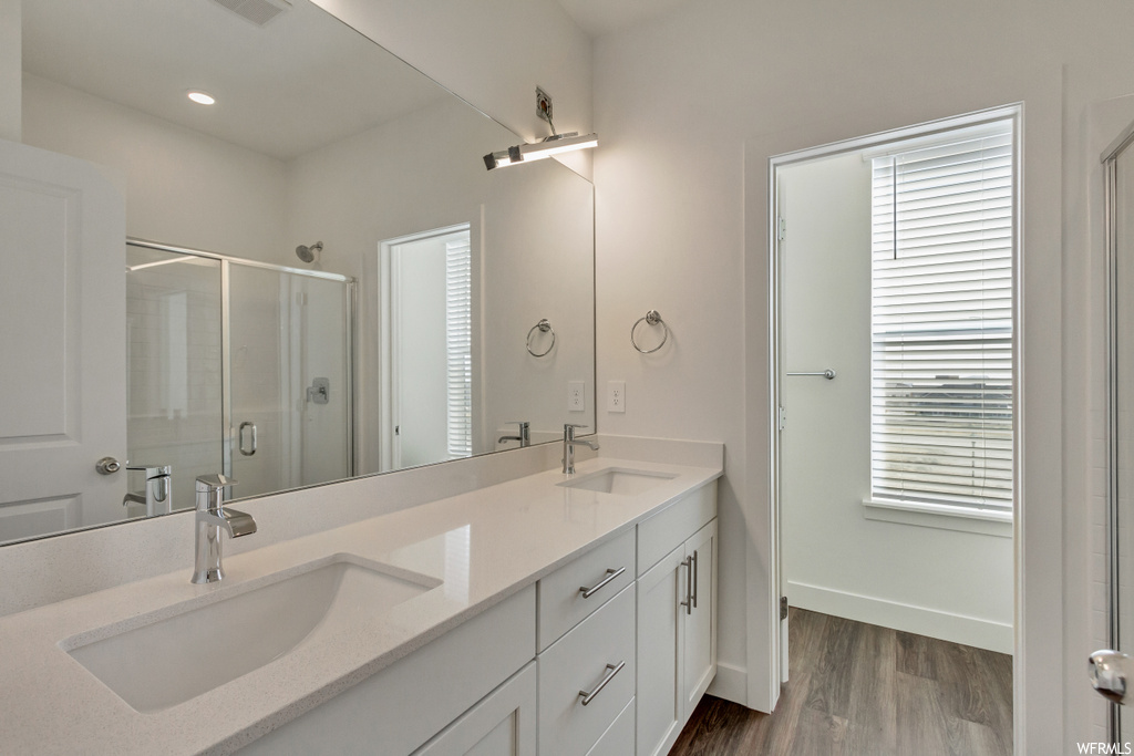Bathroom with dual vanity, a shower with door, wood-type flooring, and plenty of natural light