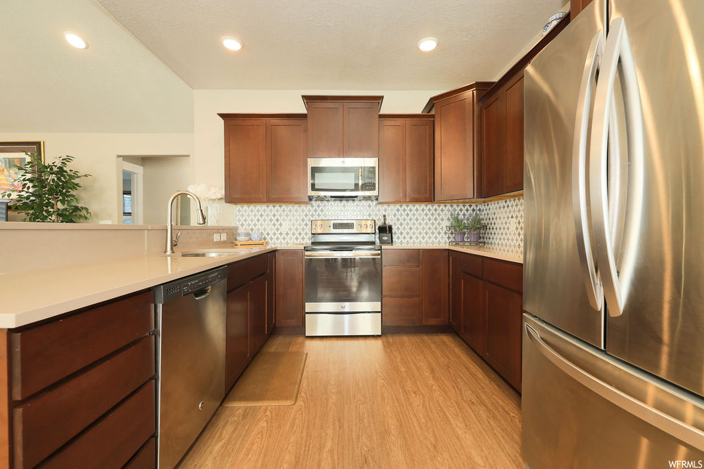Kitchen featuring backsplash, dark brown cabinets, light countertops, light hardwood flooring, and stainless steel appliances