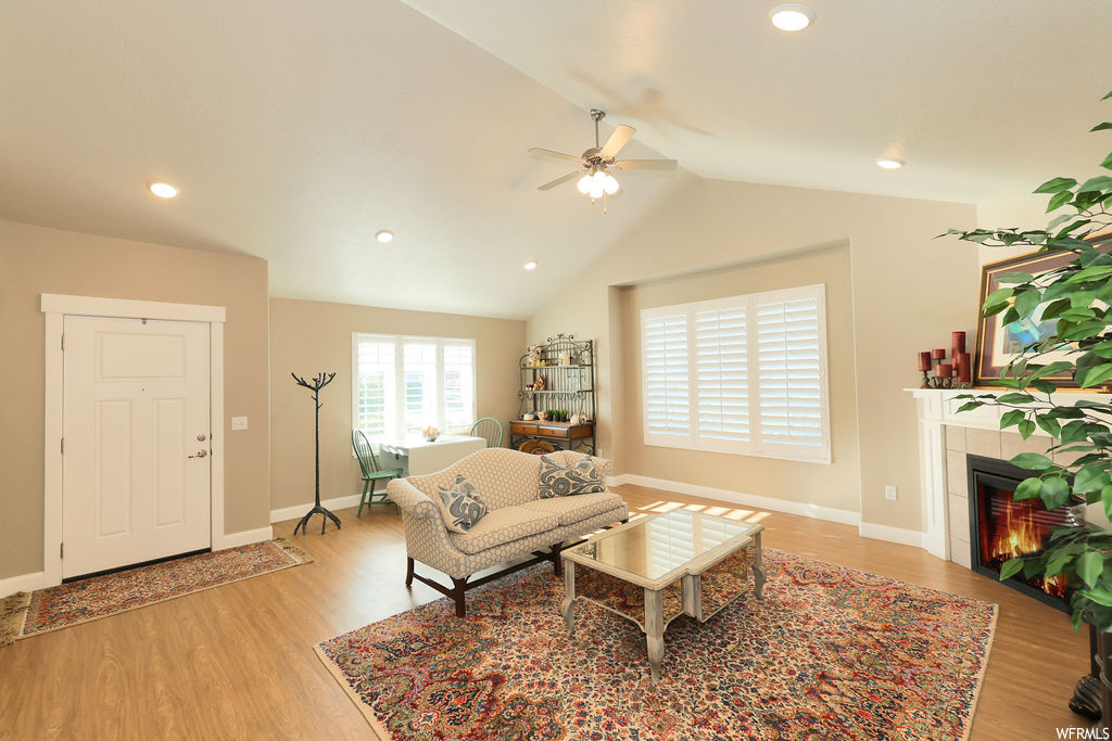 Hardwood floored living room with lofted ceiling, a fireplace, and ceiling fan