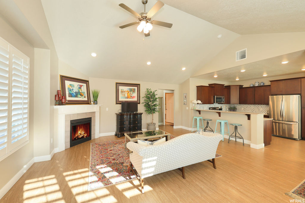 Hardwood floored living room with ceiling fan, a fireplace, a high ceiling, and lofted ceiling