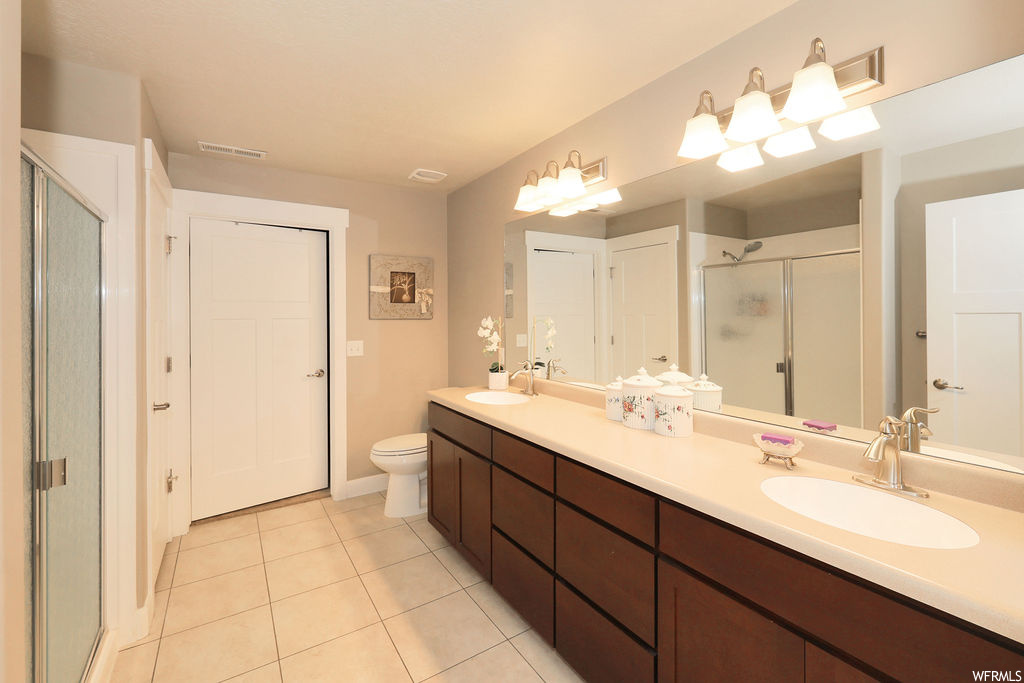 Bathroom featuring light tile floors, double sink vanity, mirror, and a shower with door