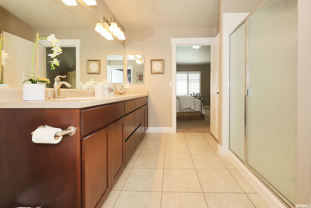 Bathroom featuring light tile flooring, mirror, a shower with door, and dual vanity