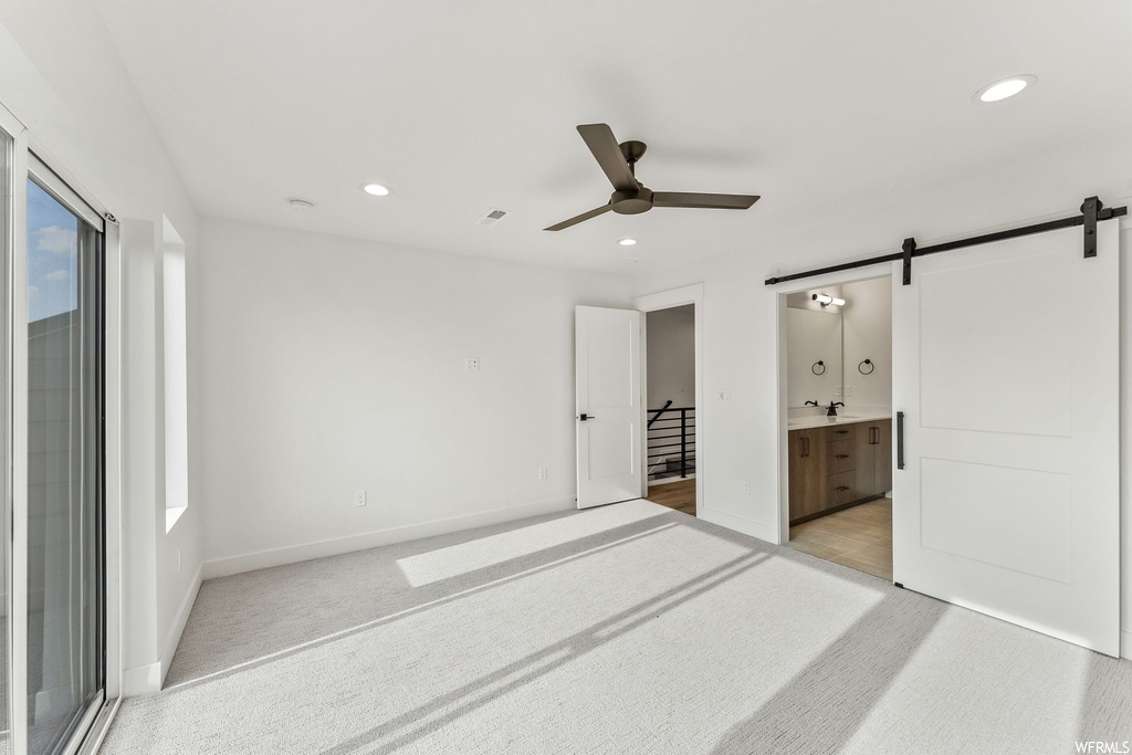 Unfurnished bedroom with light carpet, access to outside, connected bathroom, ceiling fan, and a barn door
