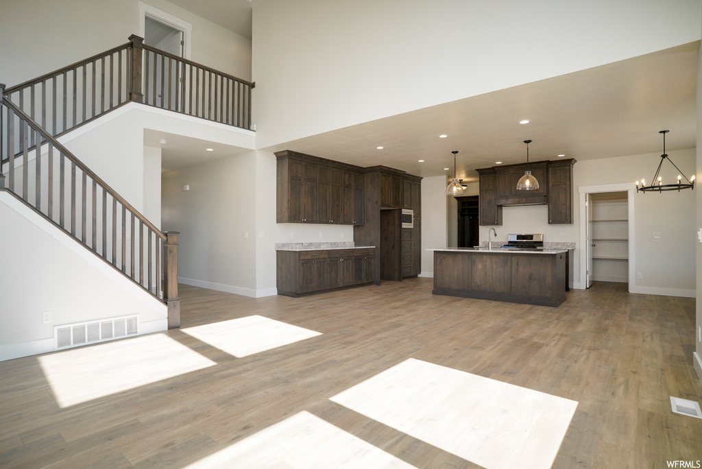 Kitchen featuring an island with sink, range, dark brown cabinetry, hanging light fixtures, light hardwood flooring, and a high ceiling