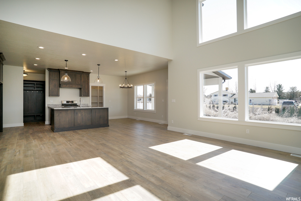 Interior space featuring range, light hardwood floors, dark brown cabinetry, pendant lighting, and a high ceiling