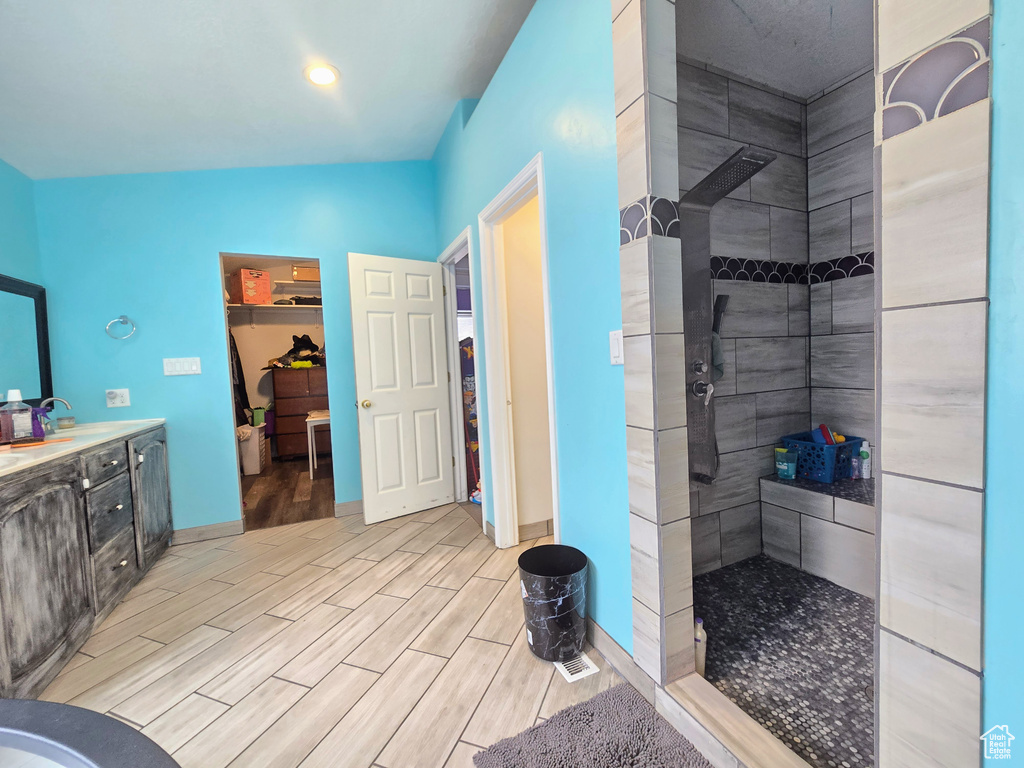 Bathroom with vaulted ceiling, hardwood / wood-style floors, vanity, and a tile shower