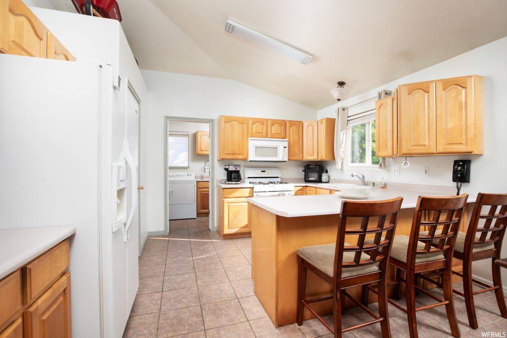 Kitchen featuring washer / dryer, a center island, light tile flooring, lofted ceiling, brown cabinets, light countertops, and white appliances