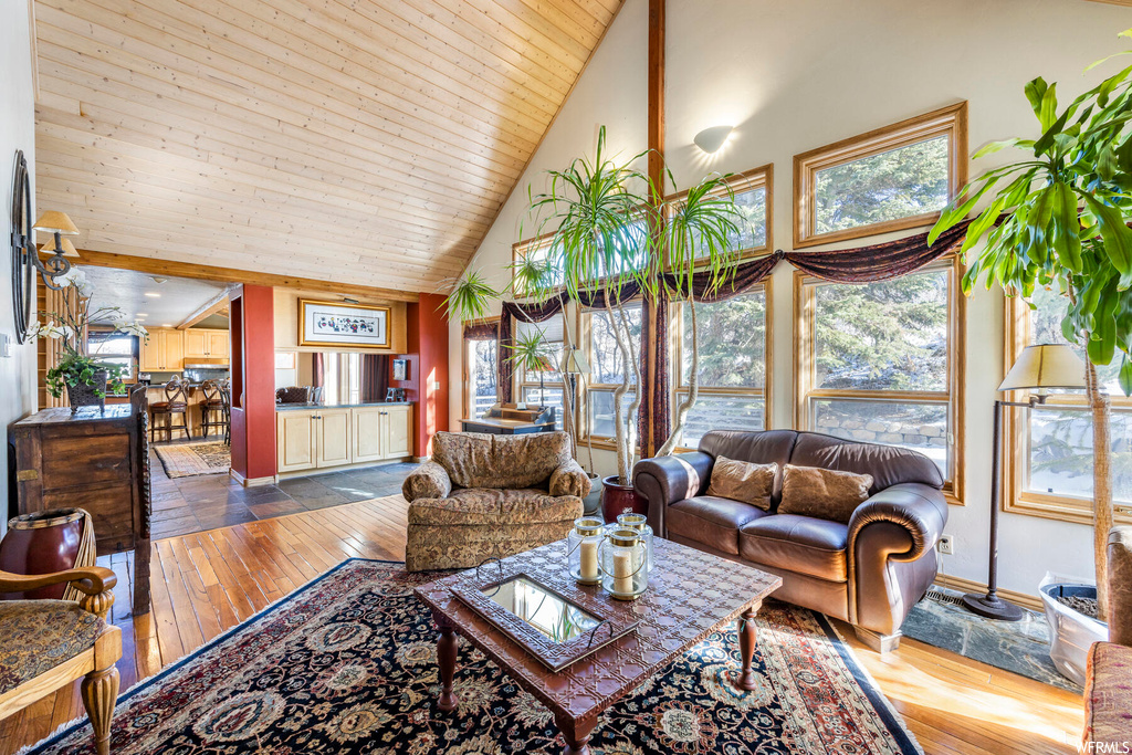 Living room featuring vaulted ceiling, a healthy amount of sunlight, wooden ceiling, light hardwood flooring, and a high ceiling