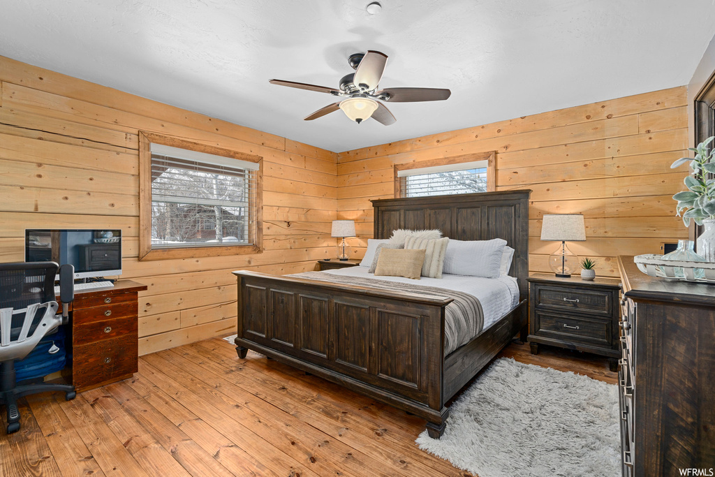 Hardwood floored bedroom featuring ceiling fan, multiple windows, and wood walls