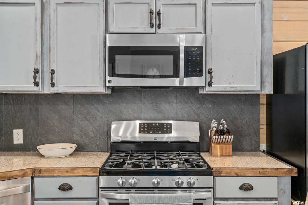 Kitchen with appliances with stainless steel finishes, backsplash, and white cabinets