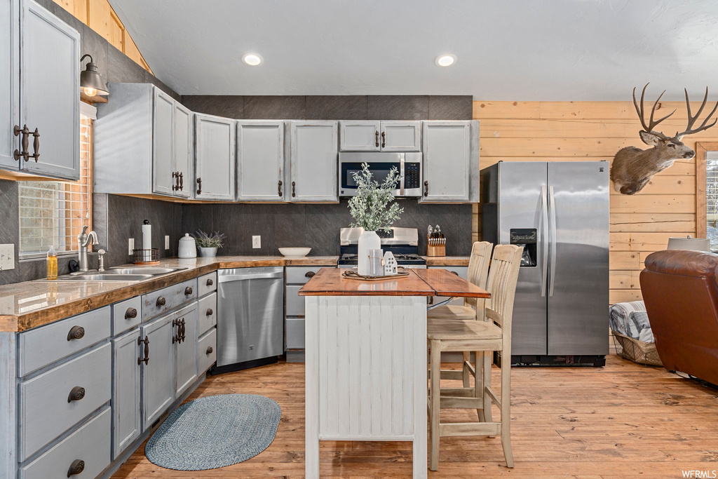 Kitchen featuring backsplash, light countertops, light hardwood flooring, stainless steel appliances, and wooden walls