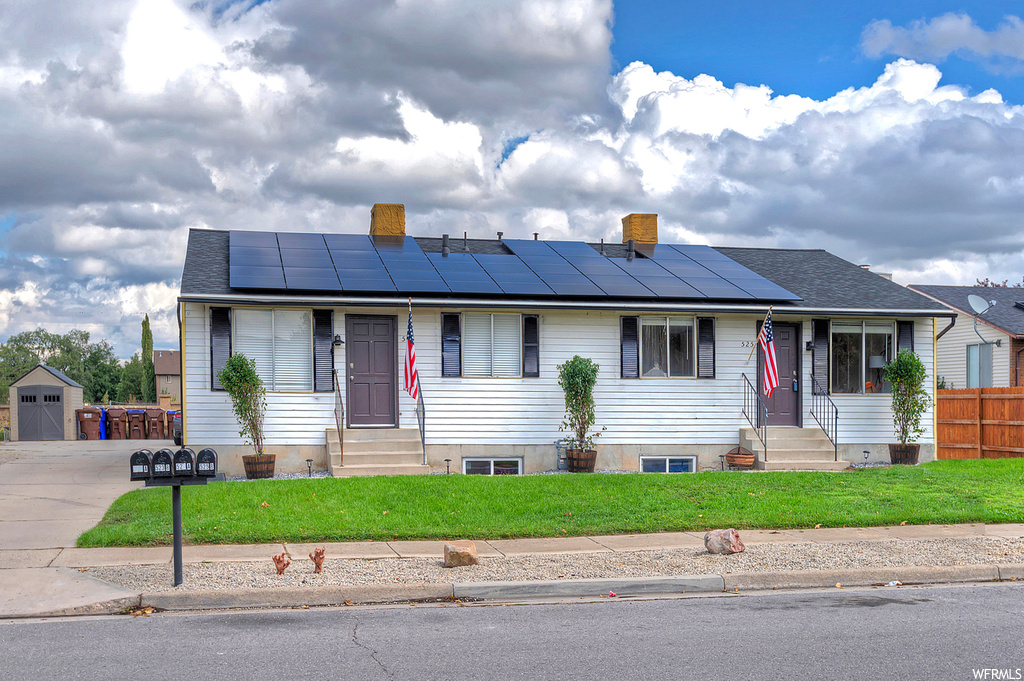 View of front of house featuring solar panels, a front lawn, and a storage shed